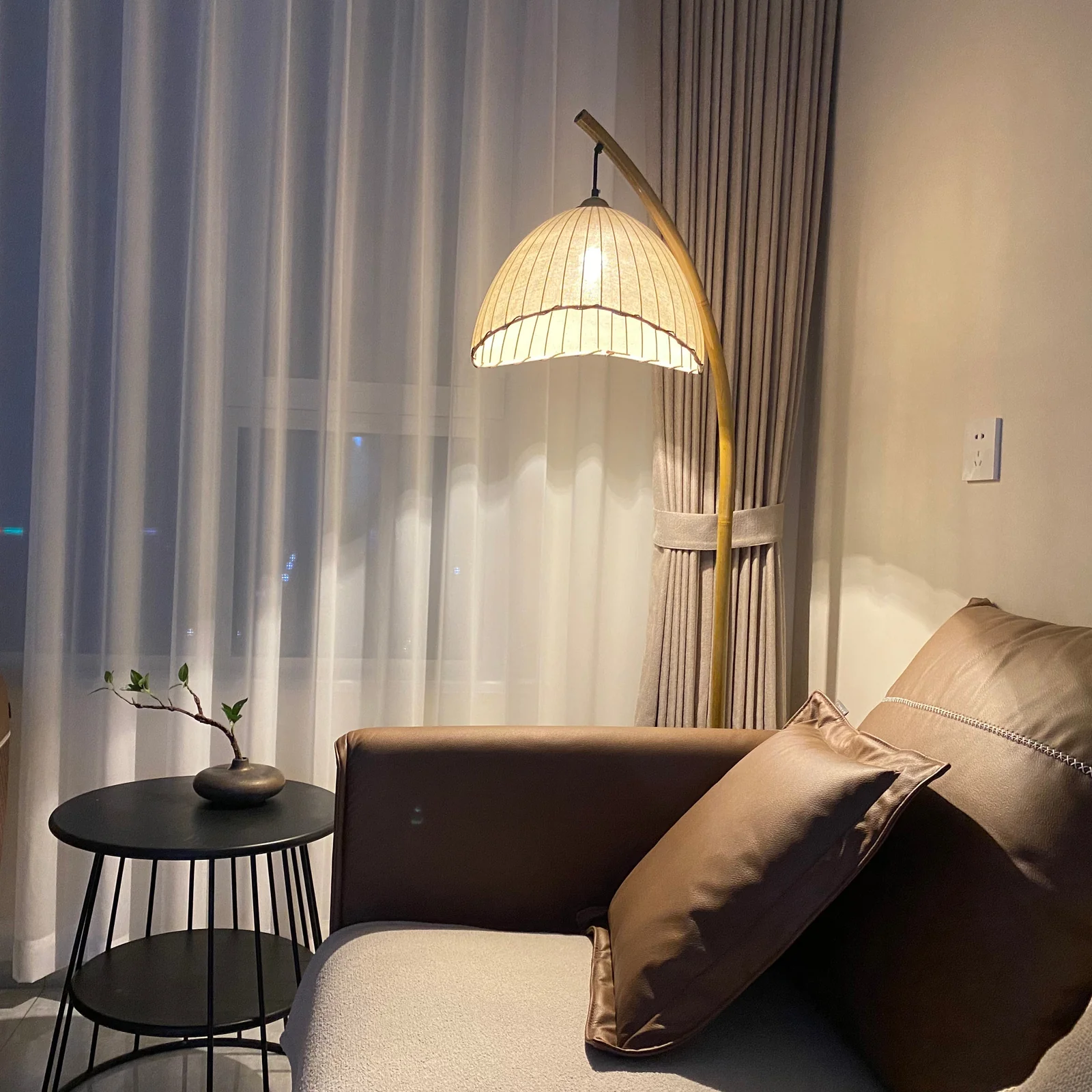 Sanna floor lamp rising beside a brown sofa and round side table in an evening living room