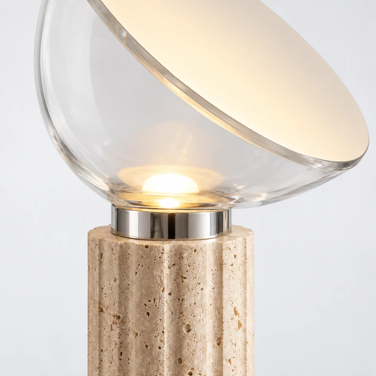Close-up of clear angled glass, silver collar, and fluted porous travertine base