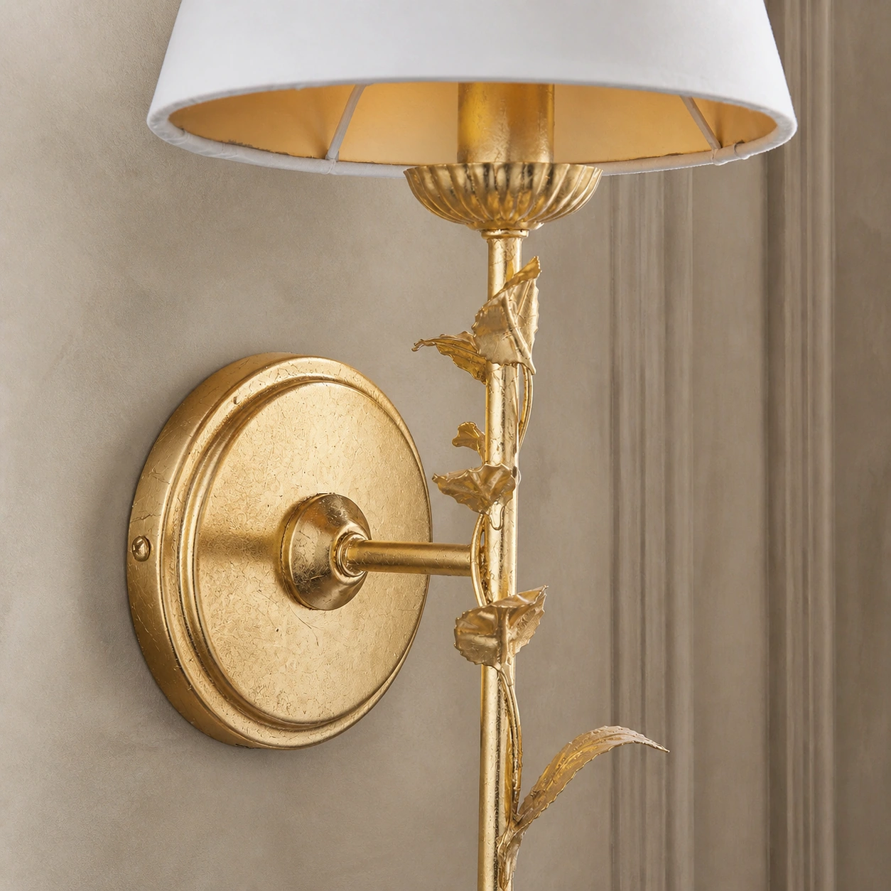 Close view of the distressed gold leaf finish across the round backplate and short wall arm