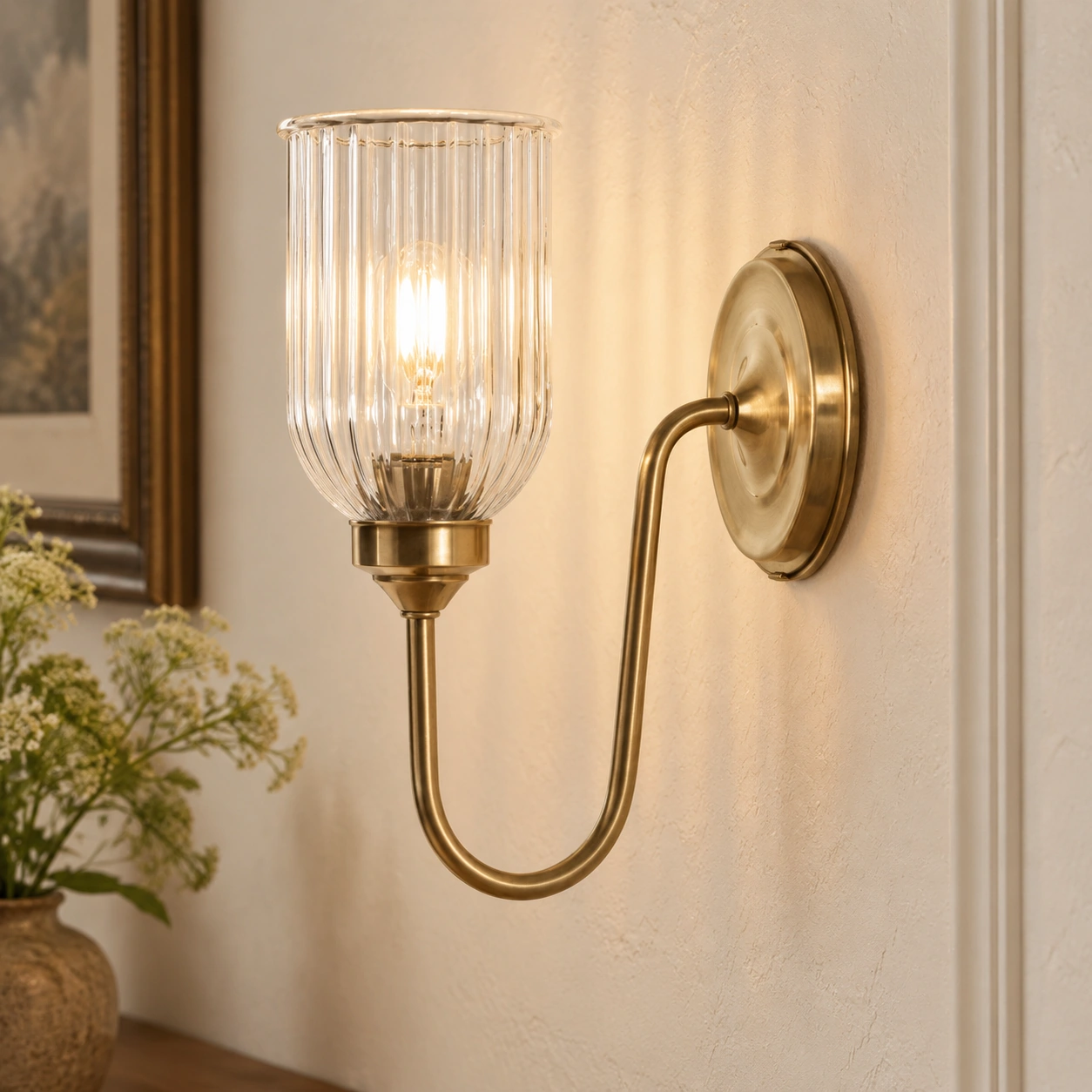 Menae wall sconce glowing through a clear ribbed glass shade against warm plaster