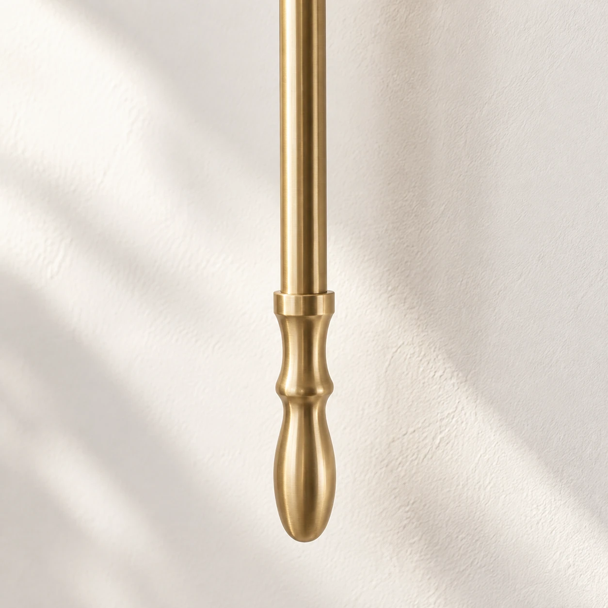 Close view of the slender brass stem and turned teardrop finial