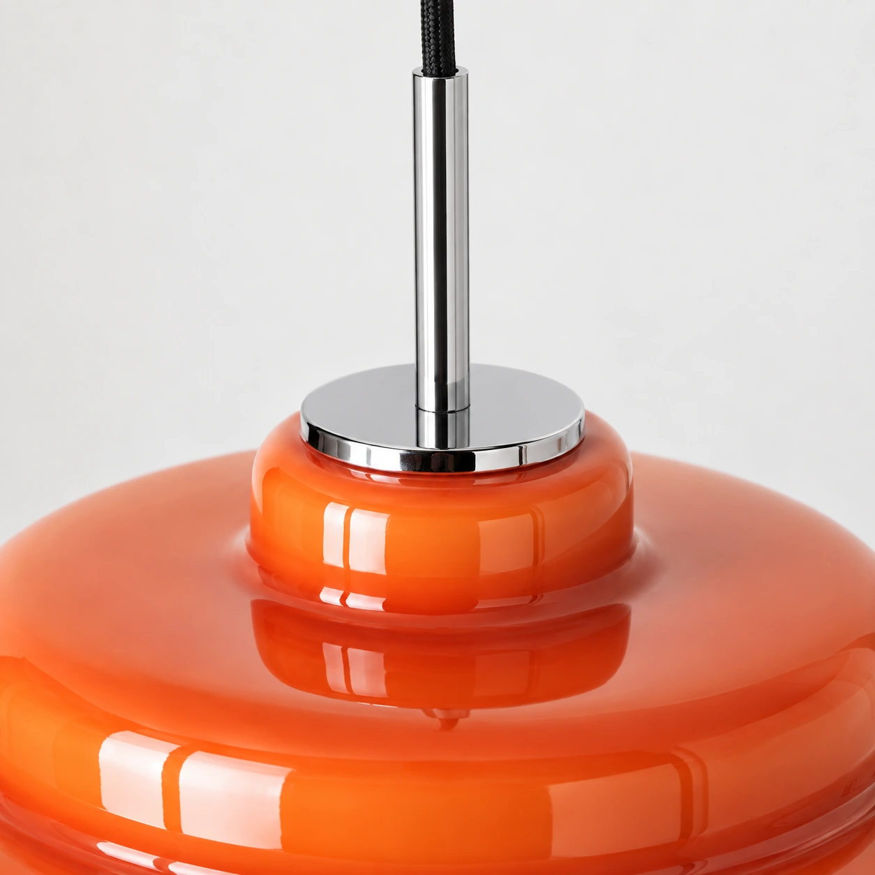 Slim chrome stem and disc connecting the orange glass shade to a black cord