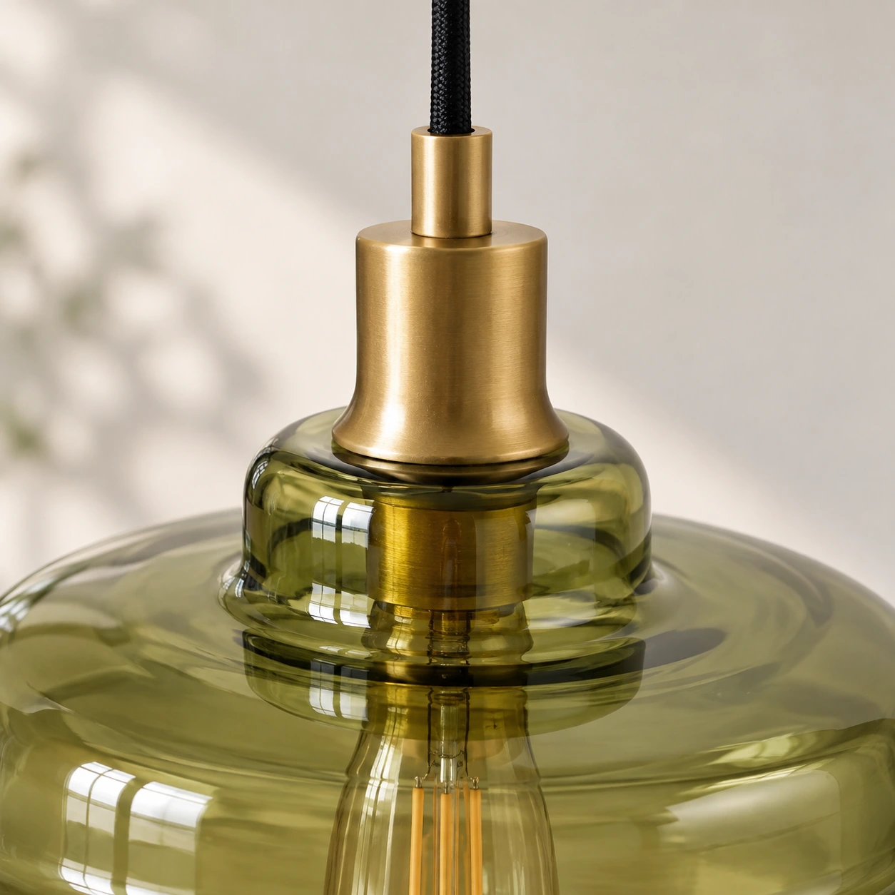 Gold-toned metal housing where the black cord meets the green glass shade