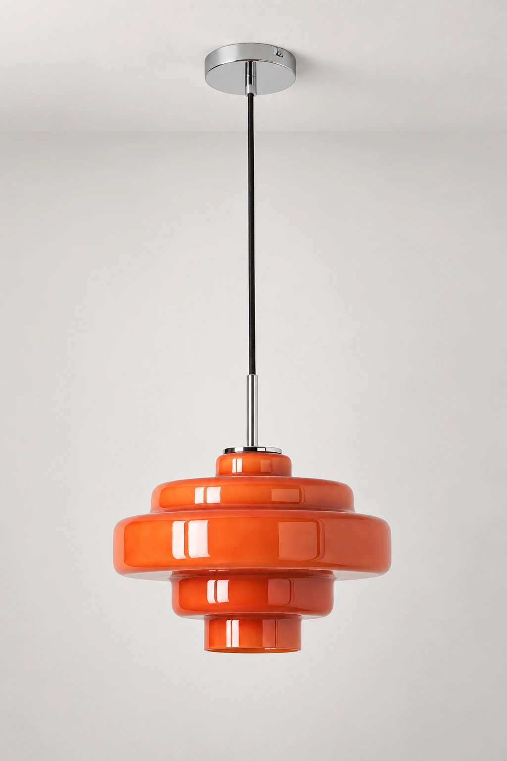 Complete orange pendant with chrome ceiling canopy, black cord, slim stem and tiered glass shade against a neutral backdrop